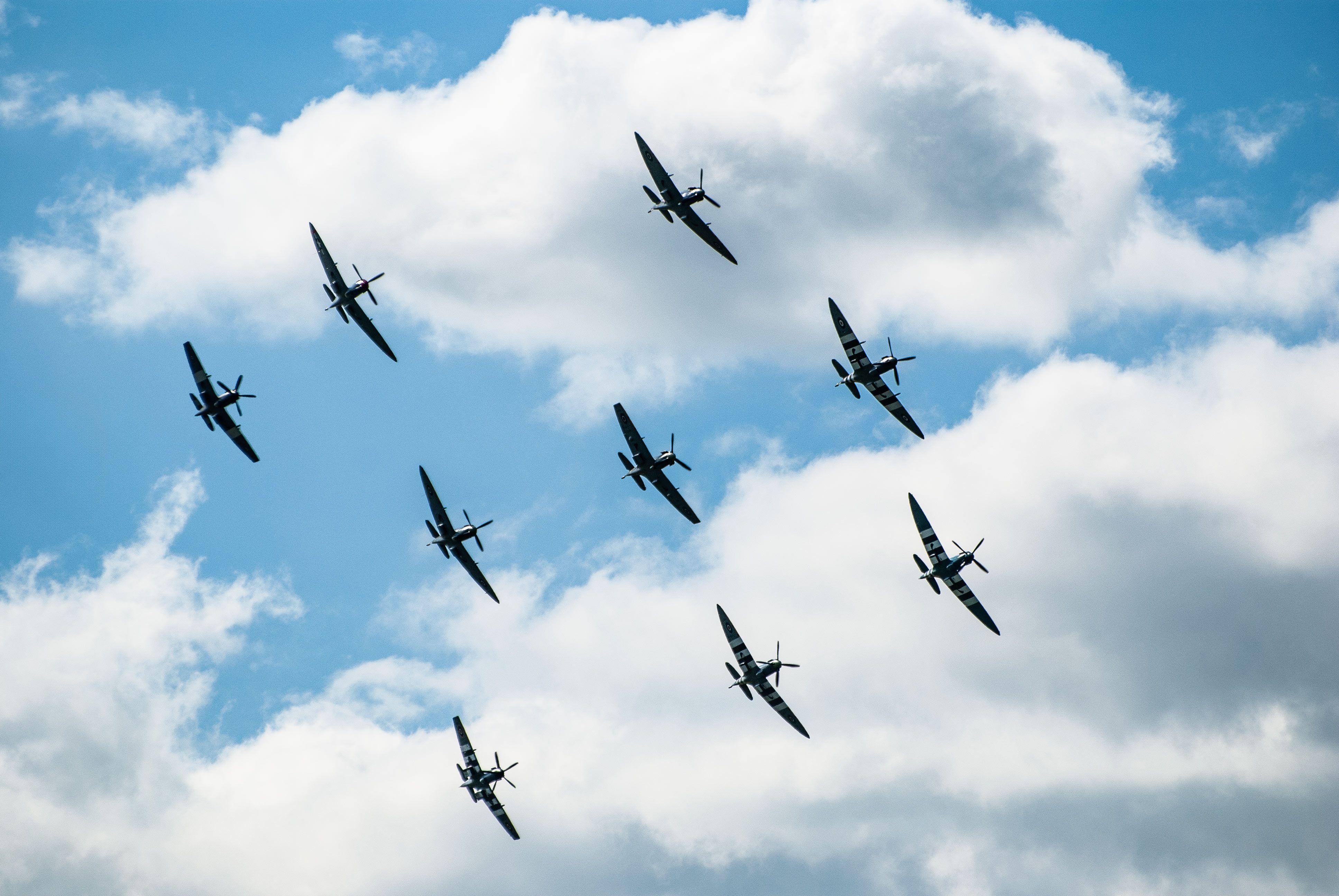 A group of vintage fighter planes flies in formation against a bright blue sky.