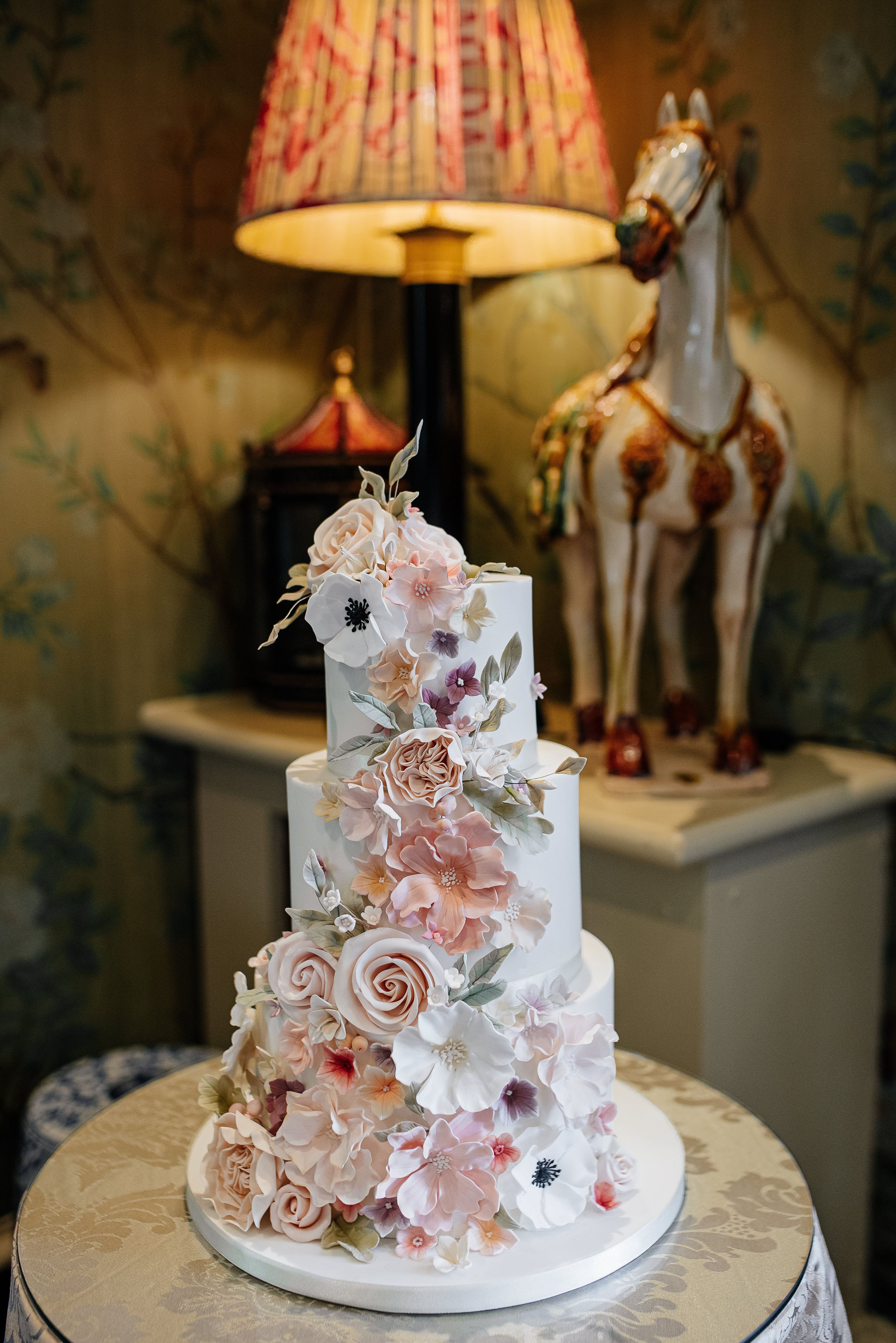 A beautifully decorated floral wedding cake set in a vintage-inspired room with soft lighting.