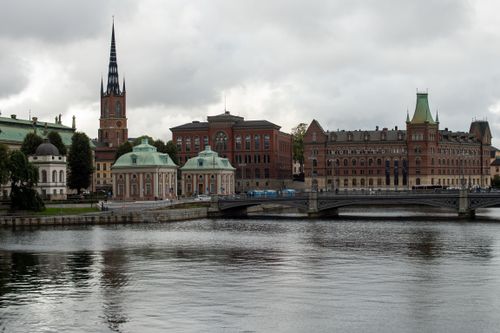 Free Explore the serene waterfront view of Stockholm with the historic Riddarholm Church and classic architecture under a moody sky. Stock Photo