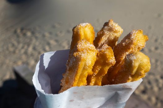 Close-up of crispy sugar-coated churros against a sandy beach background, evoking a sunny day in Montevideo.