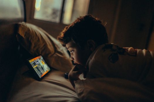 A child engrossed in watching a tablet screen in a dimly lit bedroom, creating a cozy evening ambiance.
