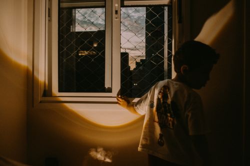 Free Child silhouetted against a window at sunset, casting a dramatic indoor shadow. Stock Photo