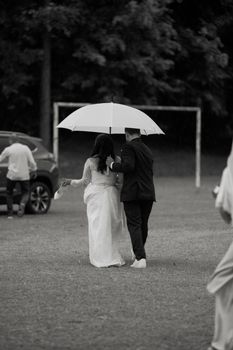 Monochrome image of a couple under an umbrella on a rainy wedding day, exuding romance.