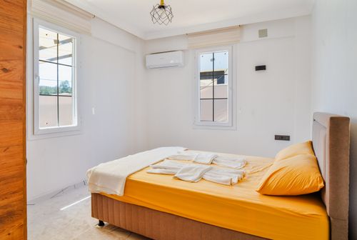 Free A neat and sunlit minimalist bedroom with warm yellow bedding and white decor. Stock Photo