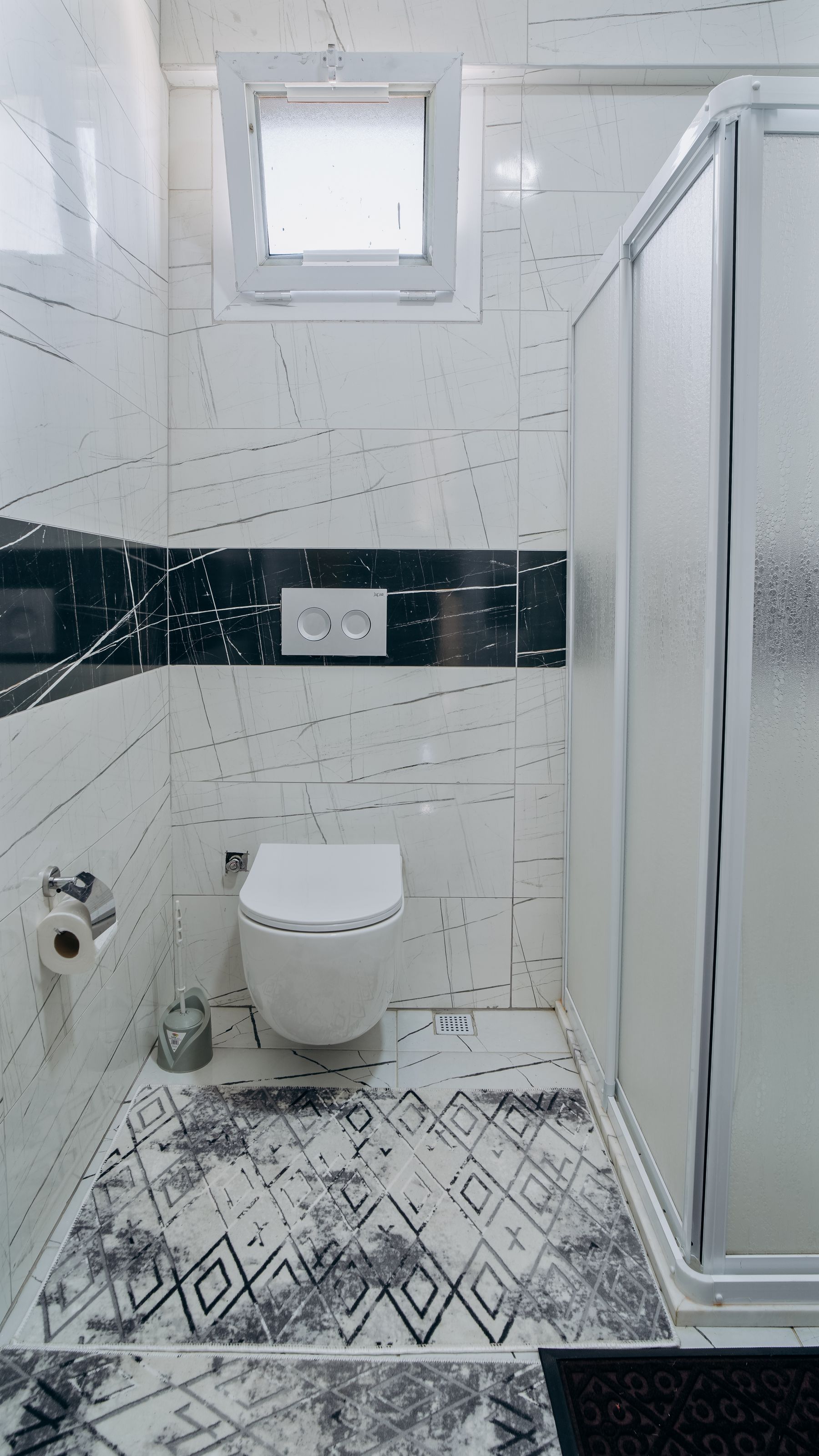 Compact modern bathroom with abstract patterned wall tile, a glass shower and white fixtures