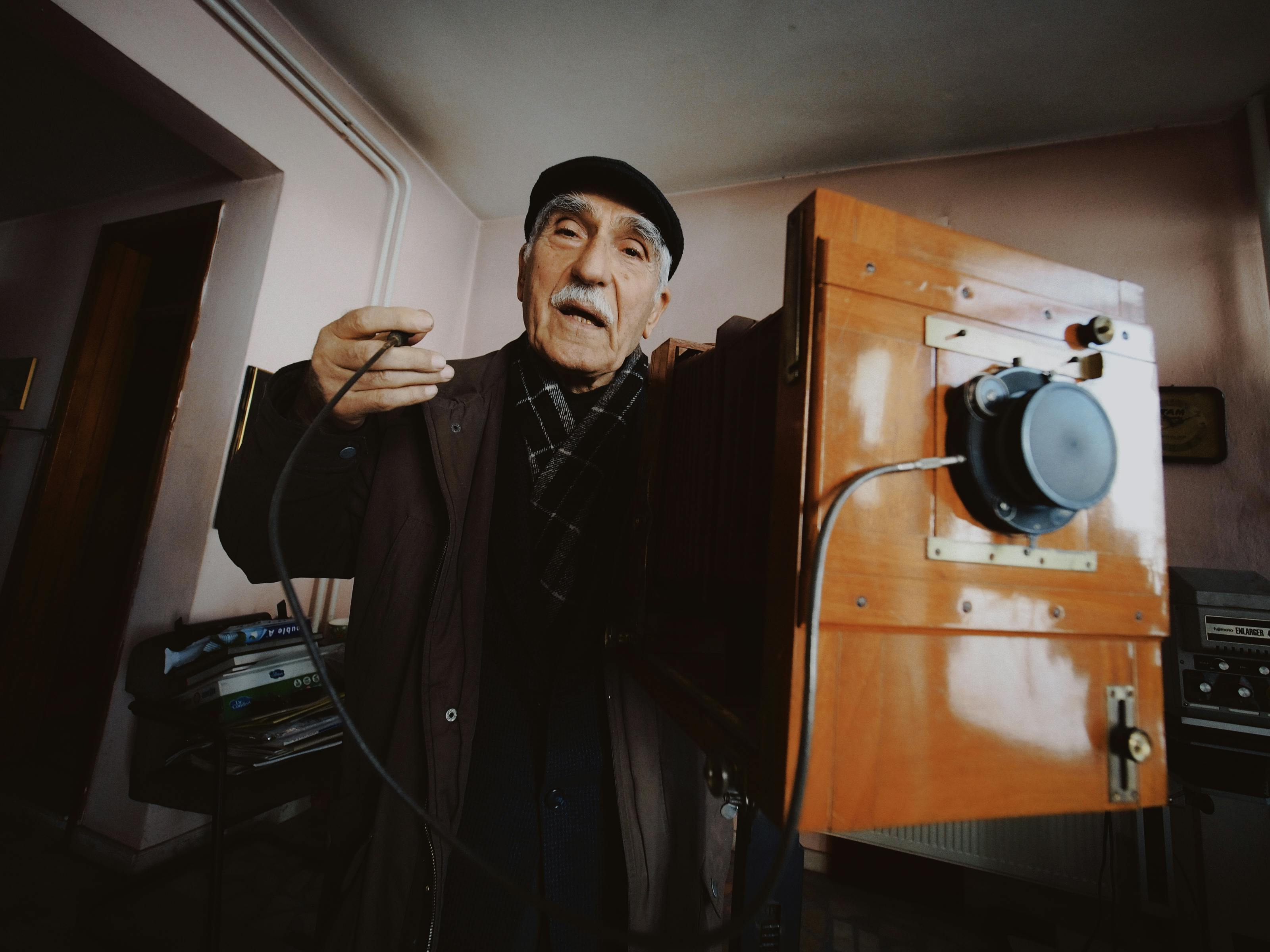 Senior man using a vintage camera indoors, showcasing timeless photography.