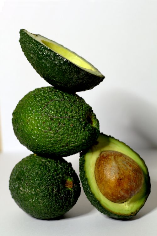 Free A creative arrangement of whole and halved avocados stacked vertically on a white backdrop. Stock Photo