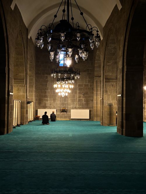Free A serene interior view of a historic mosque with elegant chandeliers and turquoise carpet. Stock Photo