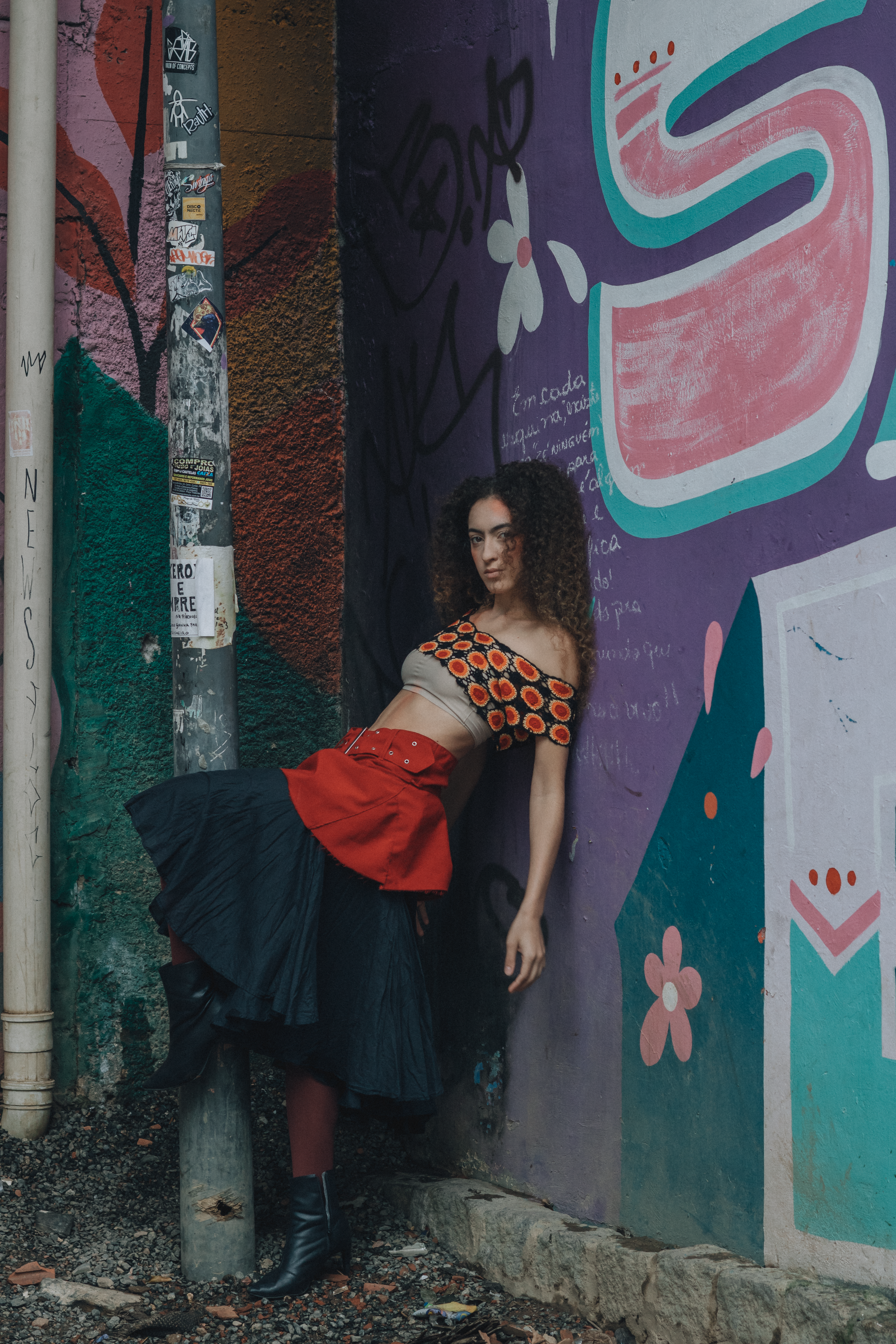 Woman in fashionable attire leans on colorful graffiti wall, showcasing urban style.