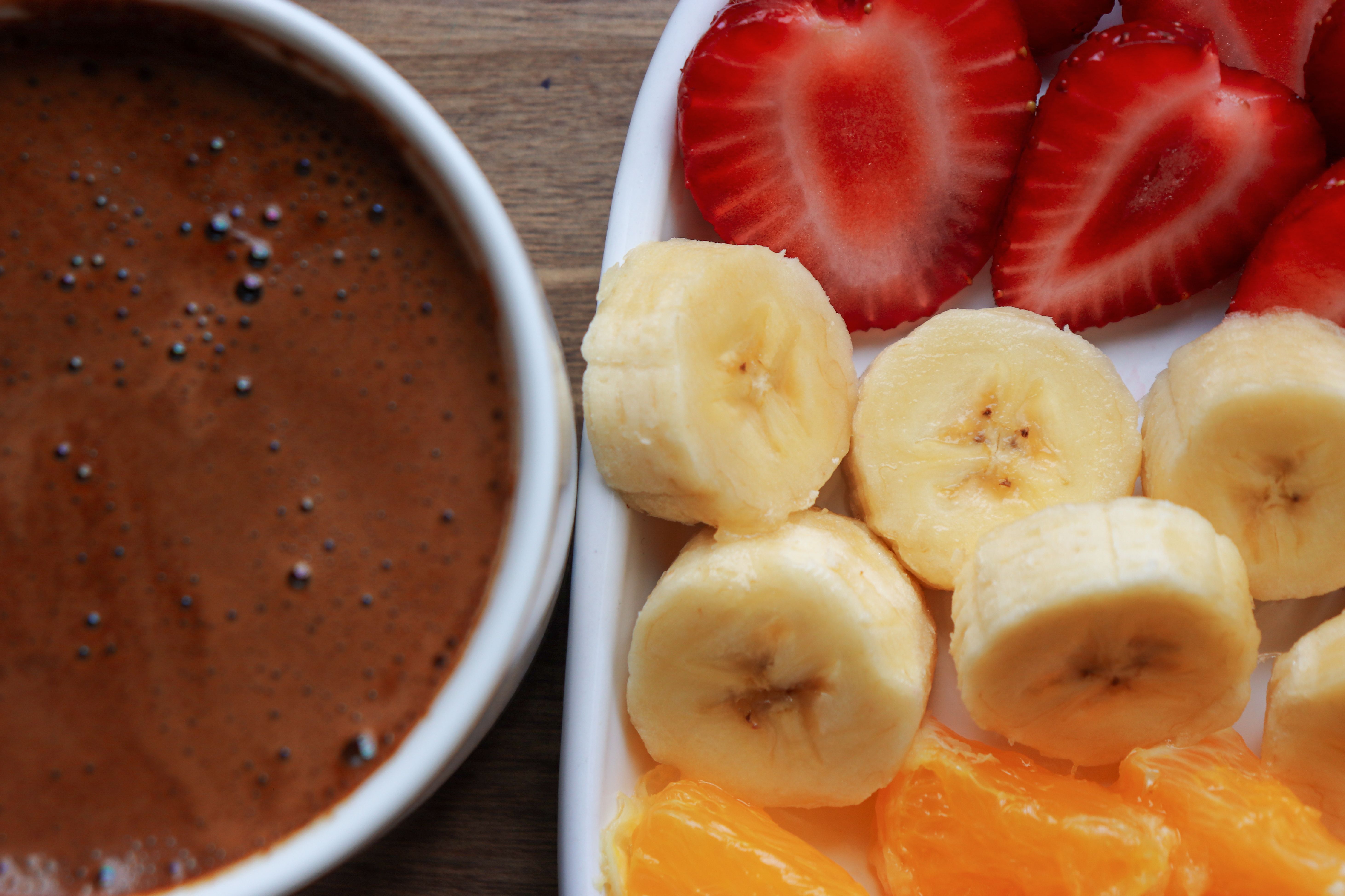 Sliced strawberries, bananas, and oranges with a bowl of rich chocolate sauce.