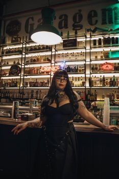 A fashionable woman poses confidently in a stylish bar with an extensive liquor selection.