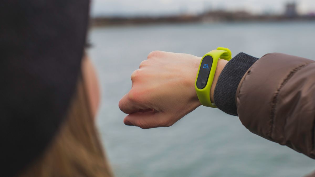 Close-up of a woman outdoors checking the time on her smartwatch by a lake.