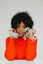 一位时尚的非裔美国女性，身着红色高领毛衣，头戴鲜花，在白色背景前摆出姿势