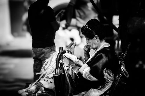 Free Candid street photo of an elderly woman sitting, reflecting deeply in a crowded area. Stock Photo