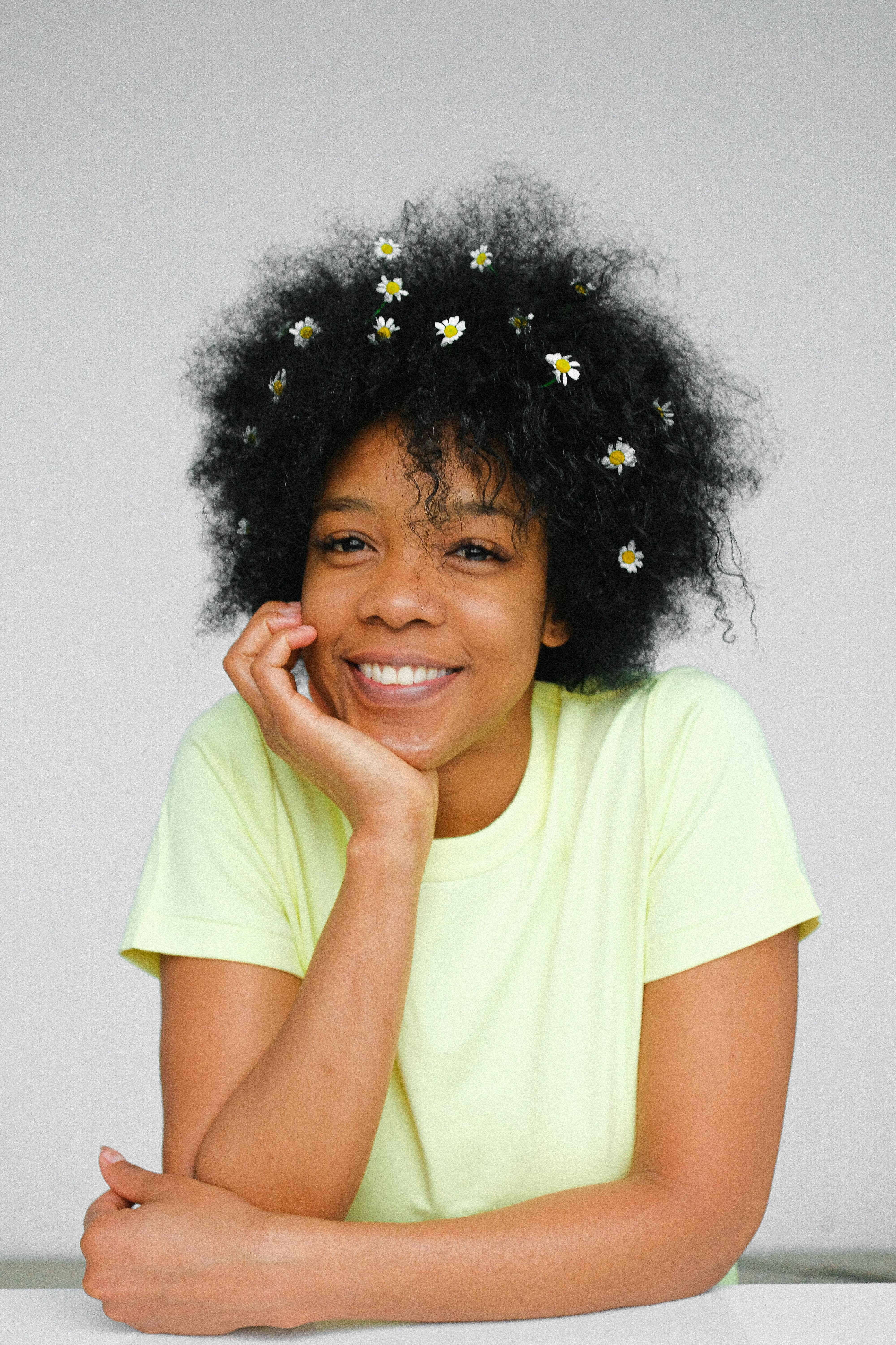 一位梳着非洲发型、头戴鲜花的微笑女子肖像，背景为白色