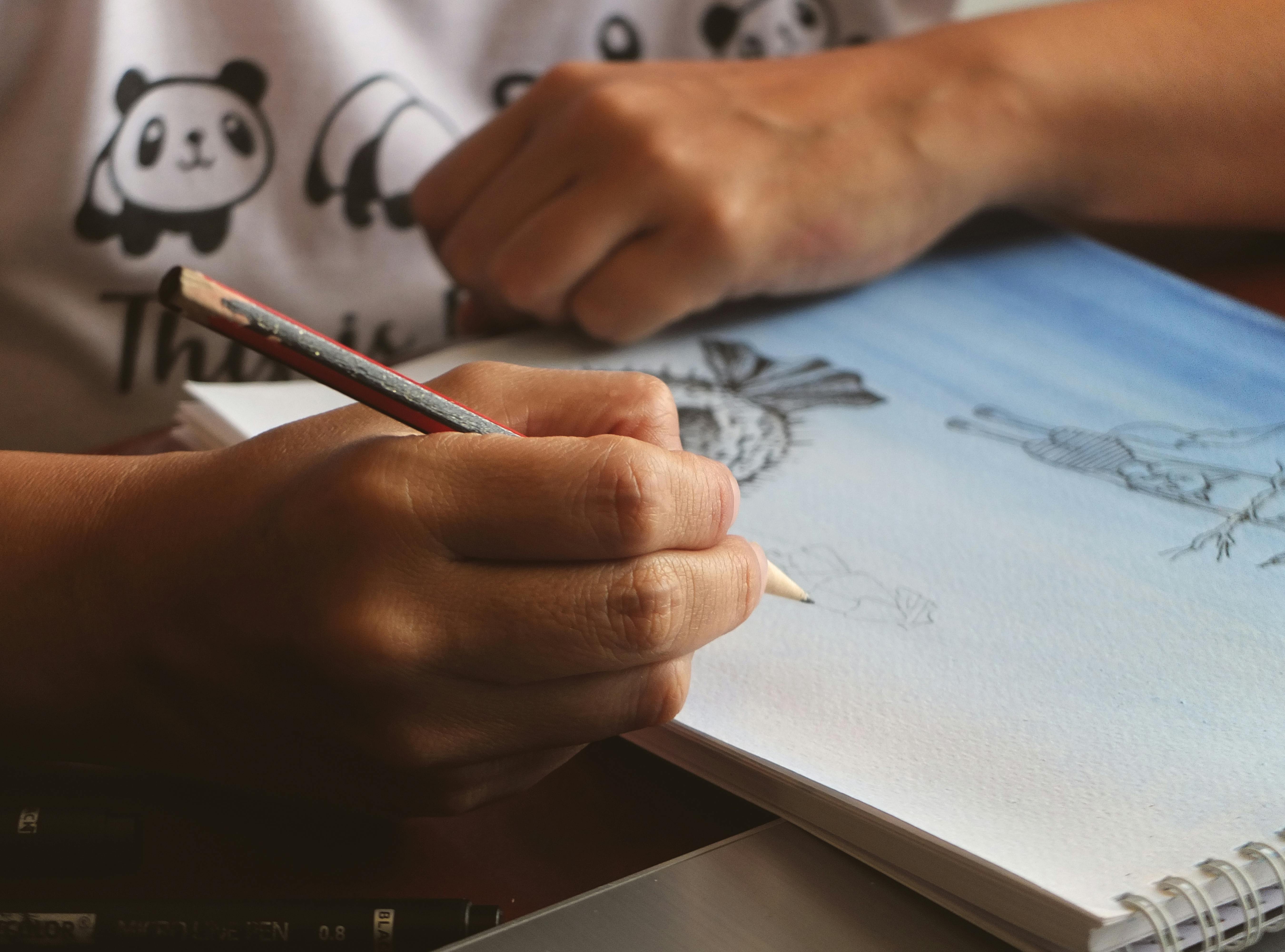 Hand sketching in a notebook with pencil, displaying artistic creativity.