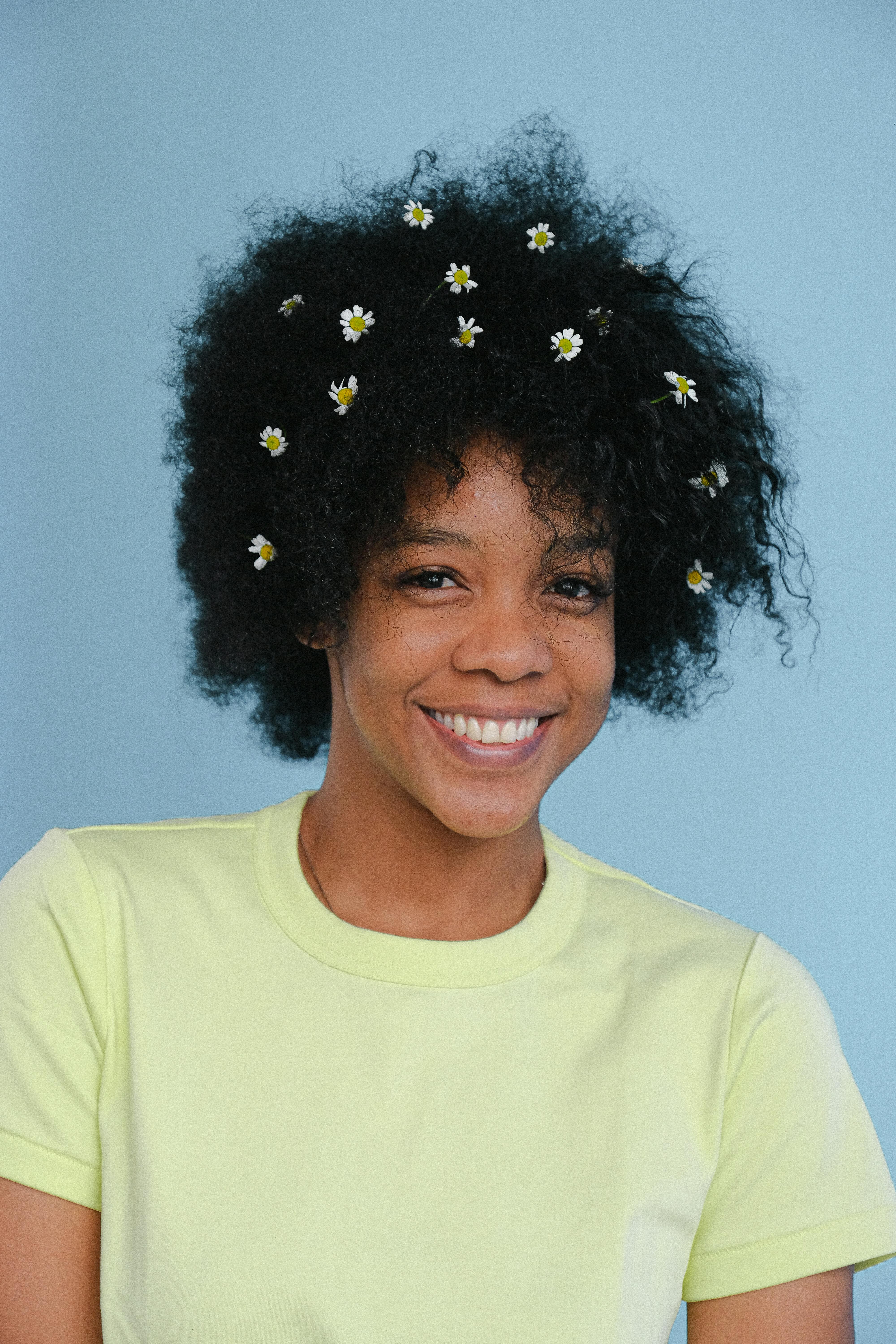 Portrait of a black woman with afro hair adorned with white flowers, smiling warmly.