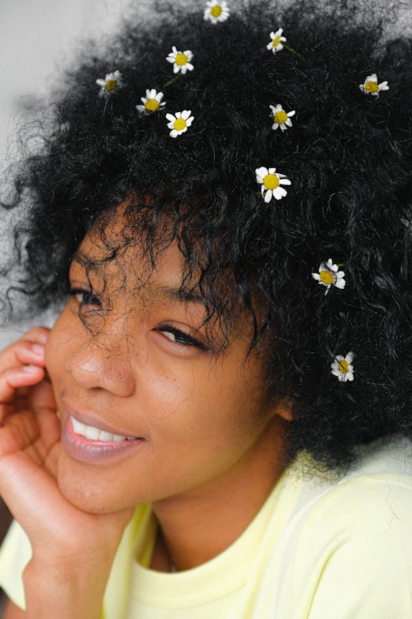 From above of wonderful tender African American woman with small chamomiles blossoms in curly hair looking away