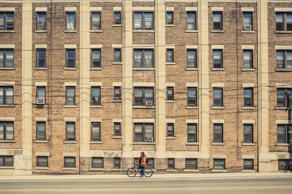 A cyclist rides past a vintage brick apartment building with a classic urban facade.
