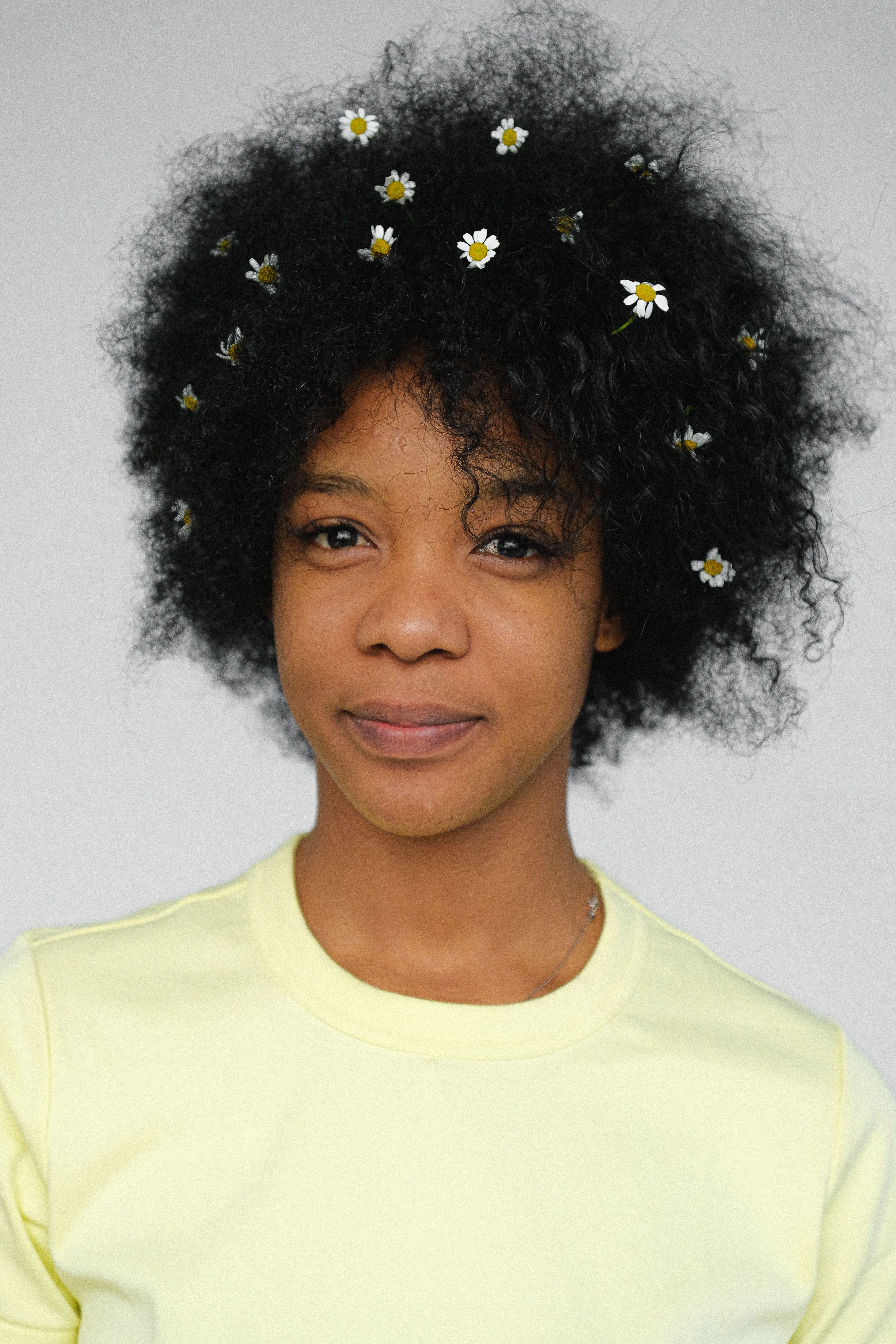 A beautiful portrait of a woman with afro hair adorned with white flowers, set against a plain background.