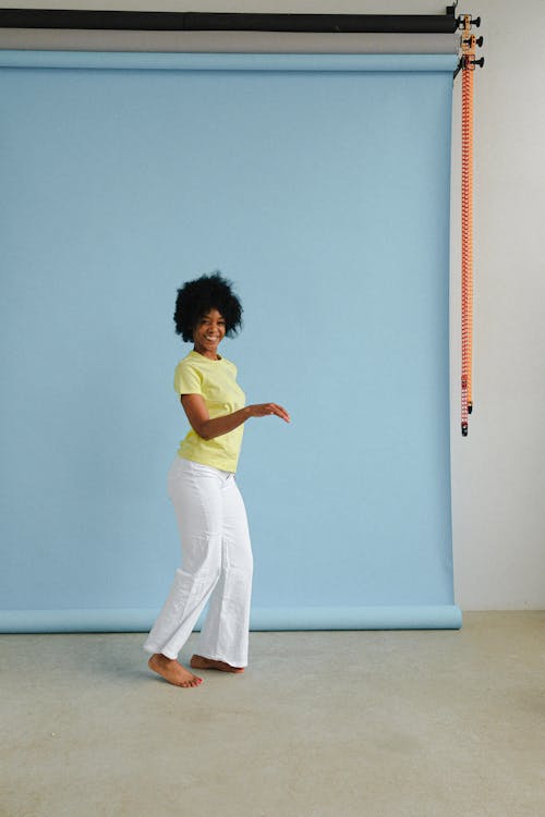Woman in Green Shirt and White Pants Standing Beside Blue Wall