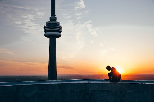 Silhouette of a Man Sitting Near Black Tower Near Body of Water during Sunset