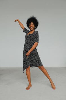 一位穿着圆点连衣裙的非裔美国女性在室内优雅地摆姿势，神情喜悦，尽显时尚