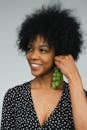 Charming black female model in polka dot dress holding bunch of grapes like earring looking away with smile