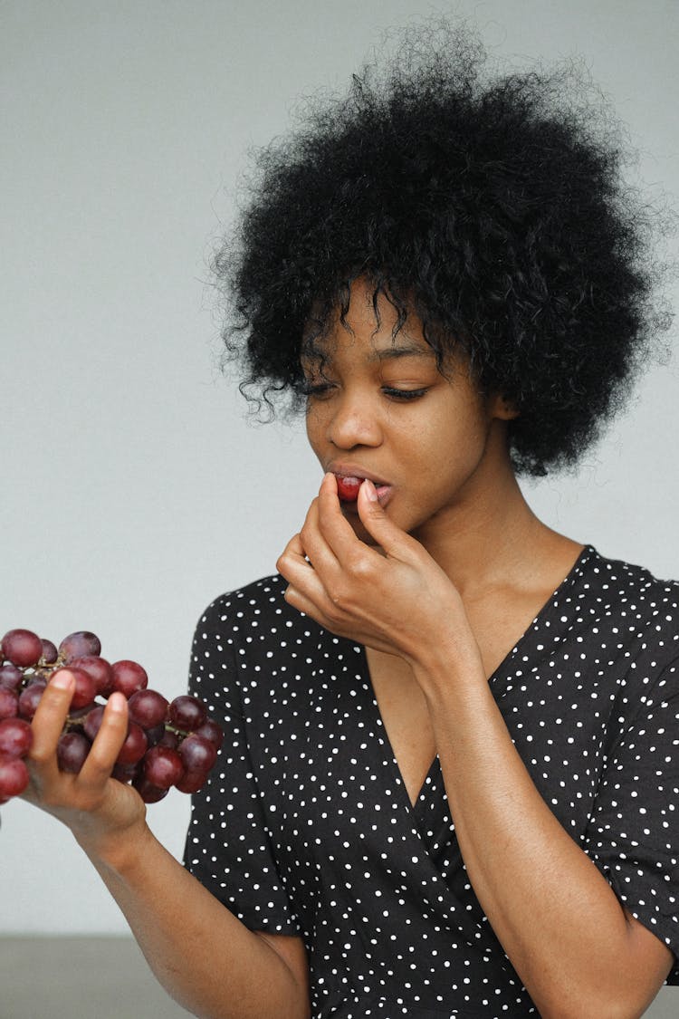 Woman In Black And White Polka Dot Shirt Holding And Eating Grapes