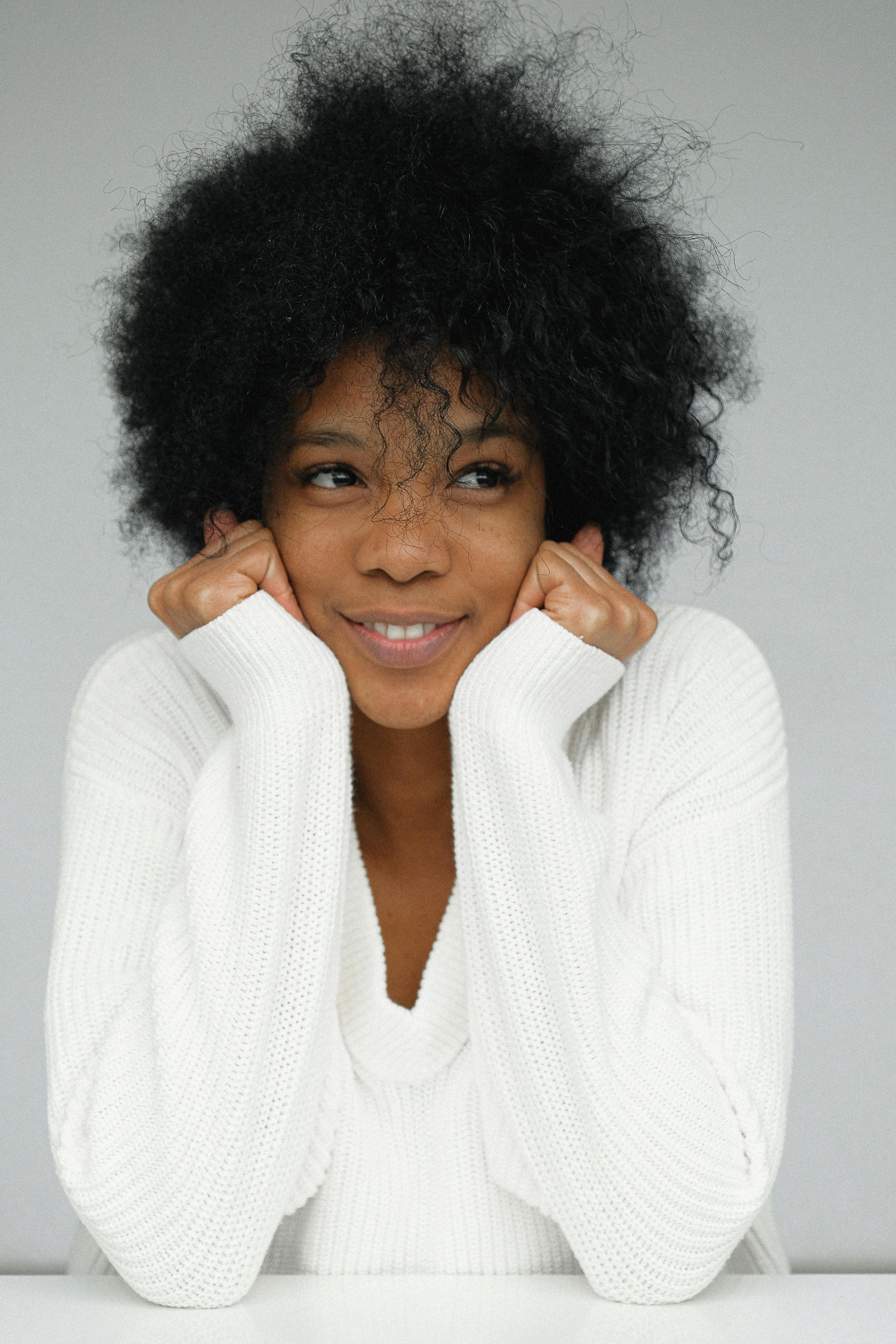 一位心满意足的女人穿着针织衫，双手托着下巴微笑，背景是灰色的