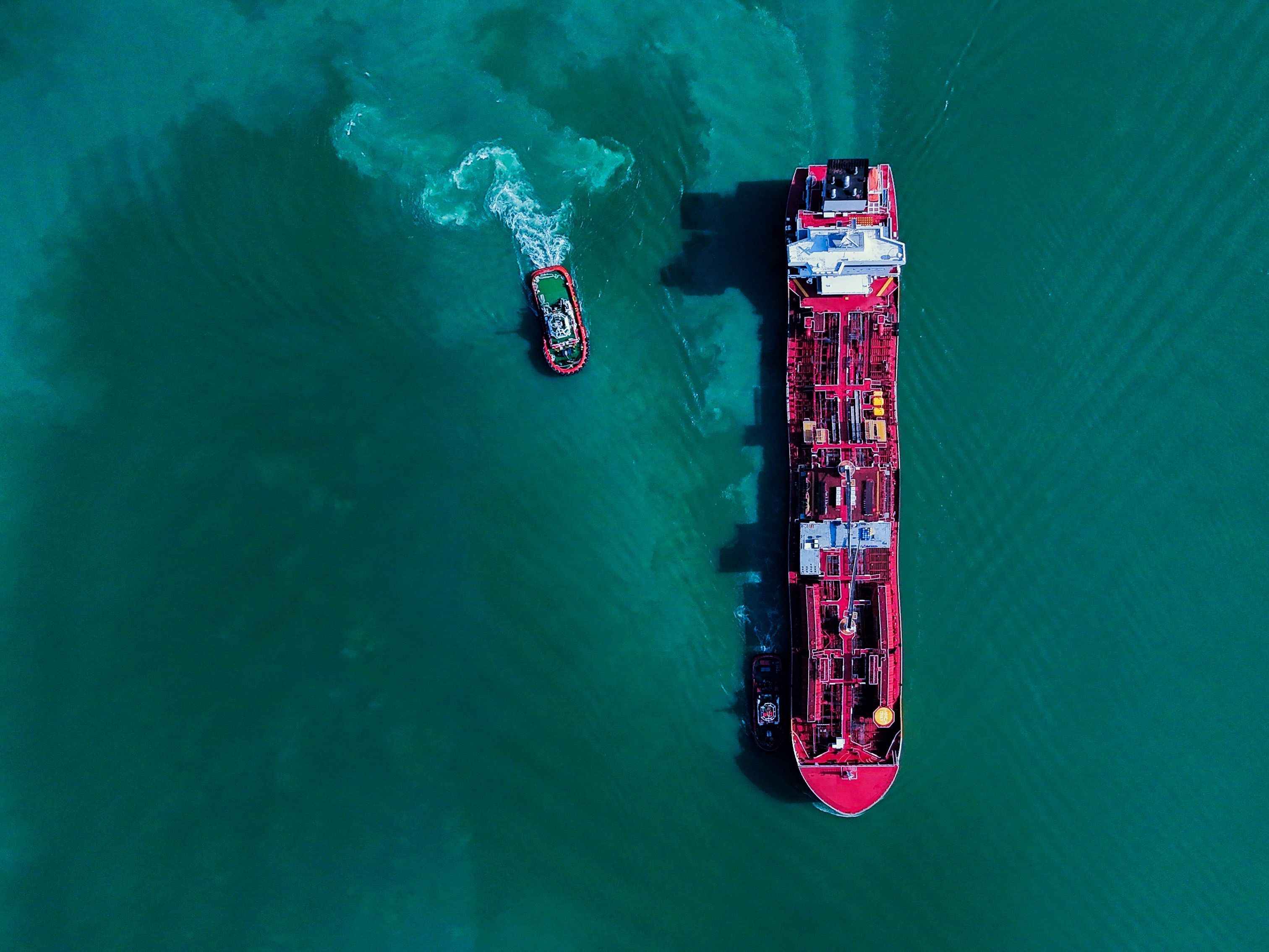 Aerial image of a vibrant red cargo ship and tugboat in the turquoise waters of Butterworth, Penang, Malaysia.