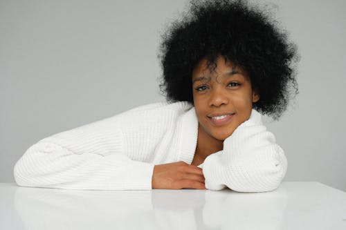 Photo of Smiling Woman in White Sweater Leaning on White Table