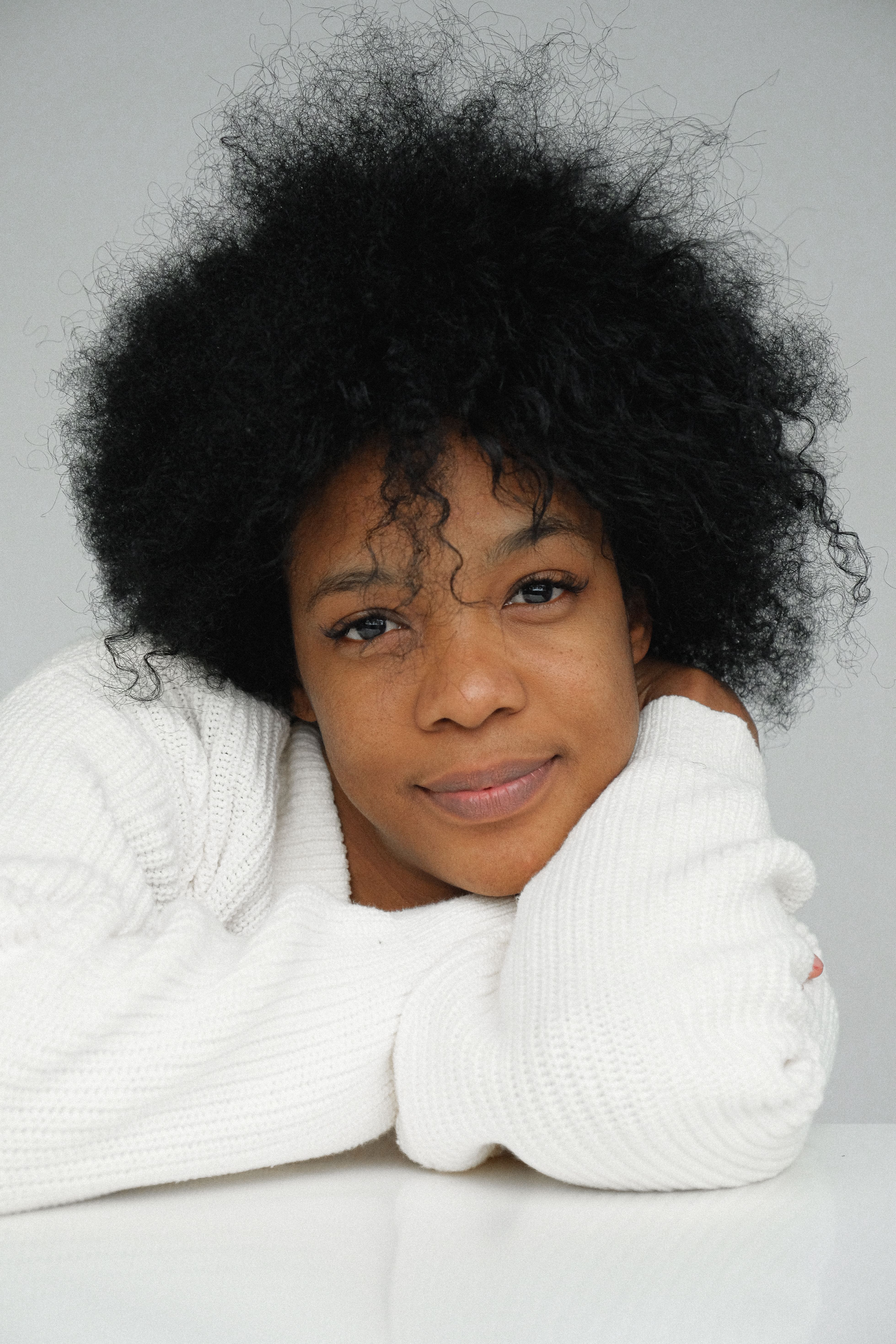 Beautiful portrait of a woman with natural afro hair, wearing a cozy white sweater.