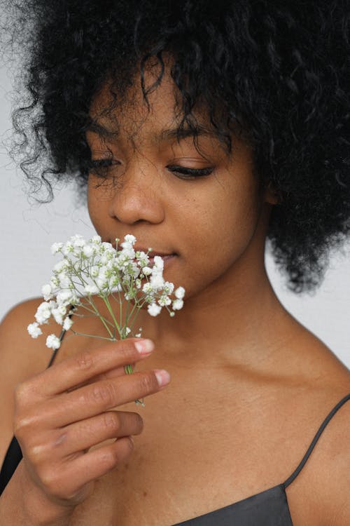 黑色意大利面条皮带顶部闻到白色花瓣花的女人的特写肖像照片