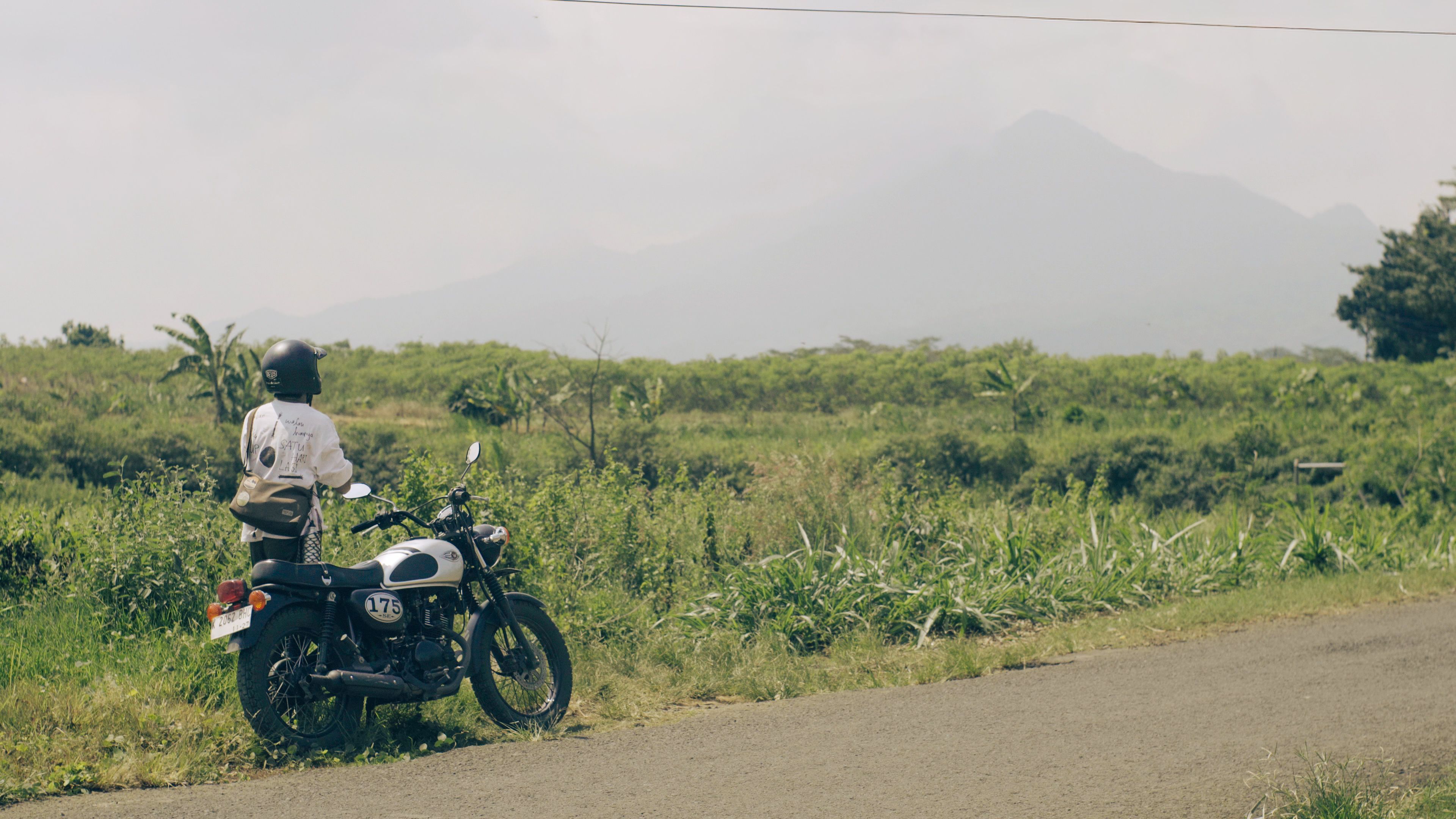 Fotomural Un motociclista hace una pausa al costado de la carretera para admirar una vista montañosa escénica bajo un cielo despejado.