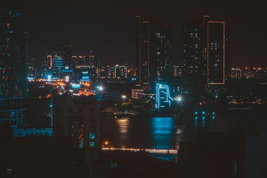 A vibrant city skyline featuring illuminated high-rise buildings and a river reflecting city lights.