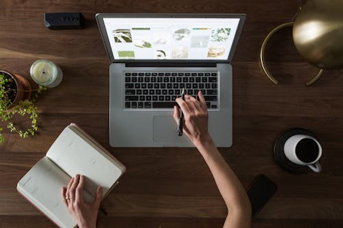 Free Person Using Macbook While Holding on Planner Book Stock Photo