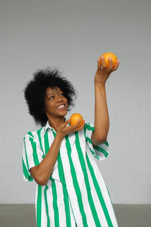 Photo of Smiling Woman in White and Green Stripe Shirt Holding up Orange Fruits