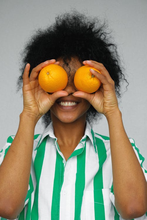 Woman in White and Green Shirt Holding Orange Fruits