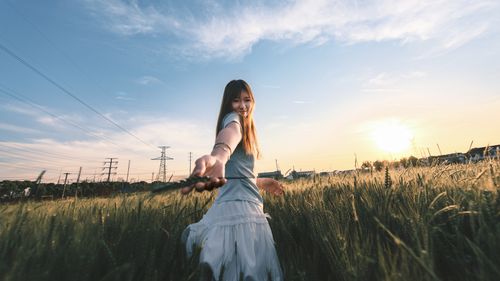 Free A young woman extends her hand in a wheat field during sunset, creating a warm and inviting atmosphere. Stock Photo