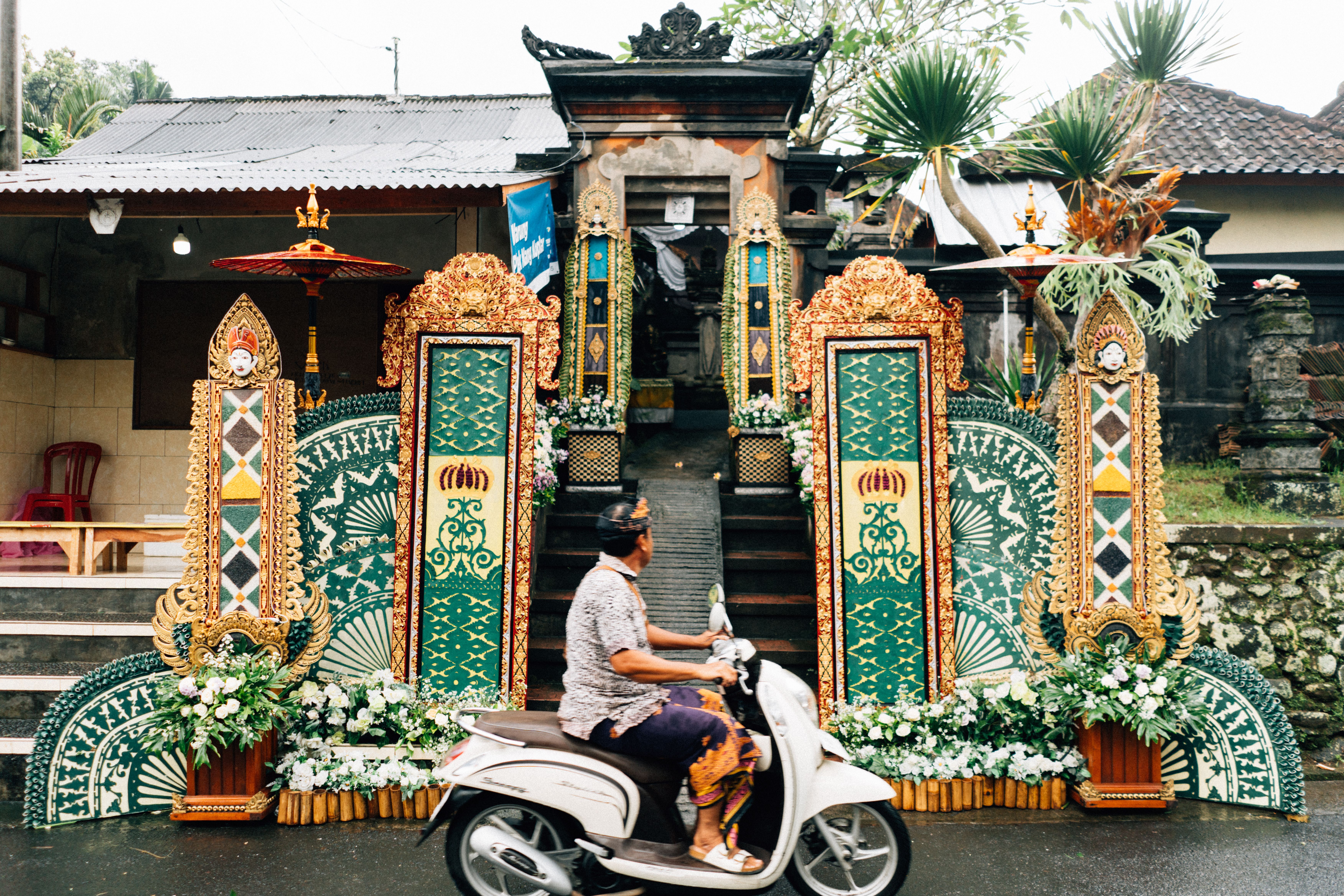 A rider on a scooter passing a Balinese temple gate, the cheapest way to get around Bali