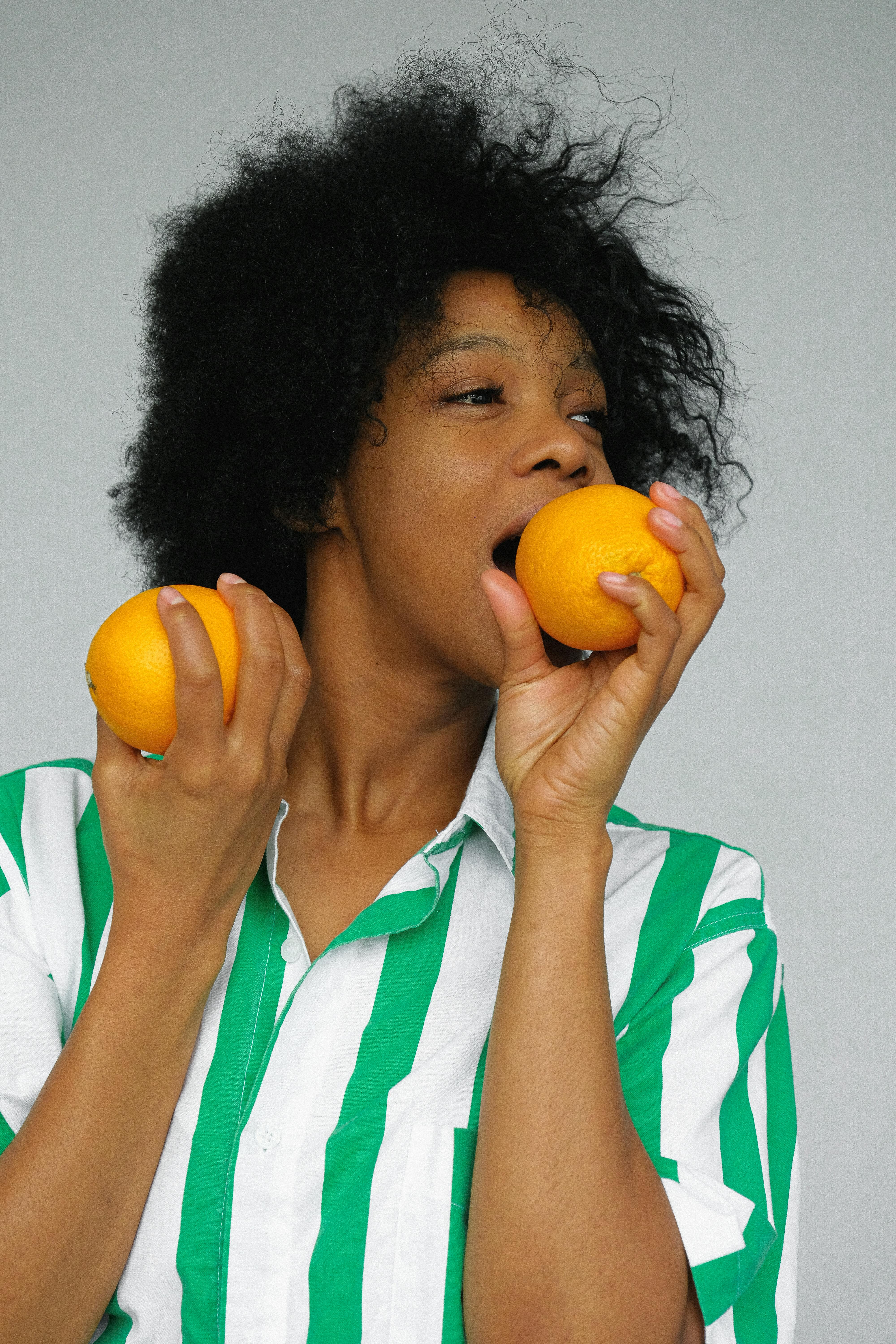 一位穿着条纹衬衫的女人在灰色背景下品尝着新鲜橙子