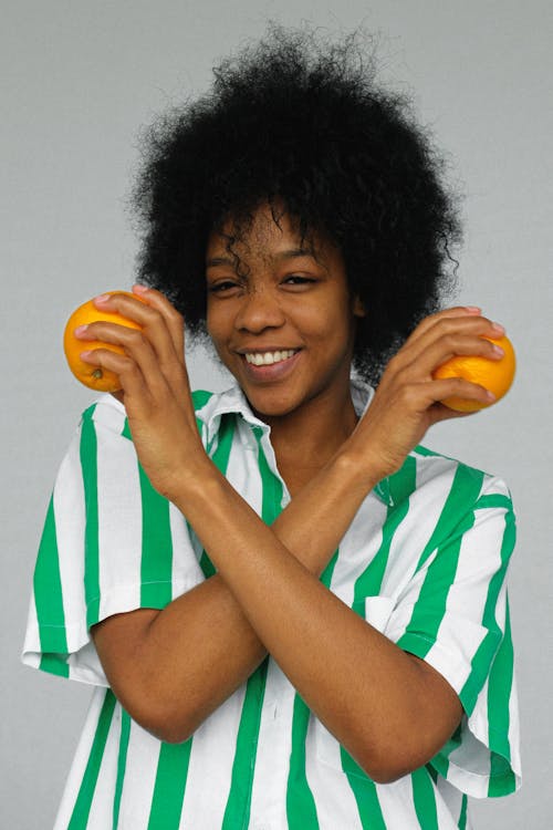 拿著橙色果子的白色和藍色條紋襯衣的微笑的婦女