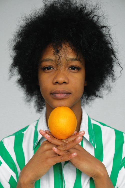 오렌지 과일을 들고 녹색과 흰색 셔츠에 여자