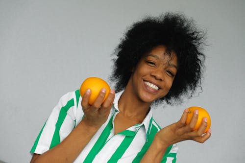 Smiling Woman in Green and White Stripe Polo Shirt Holding Orange Fruit