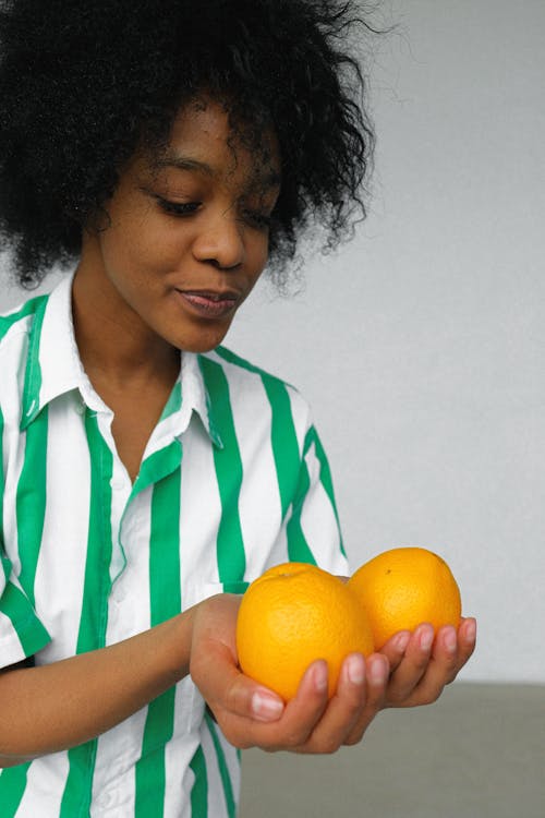 Photo of Woman in White and Green Stripe Shirt Holding Orange Fruits