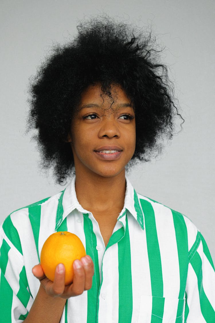 Portrait Photo Of Woman In White And Green Striped Shirt Holding An Orange Fruit