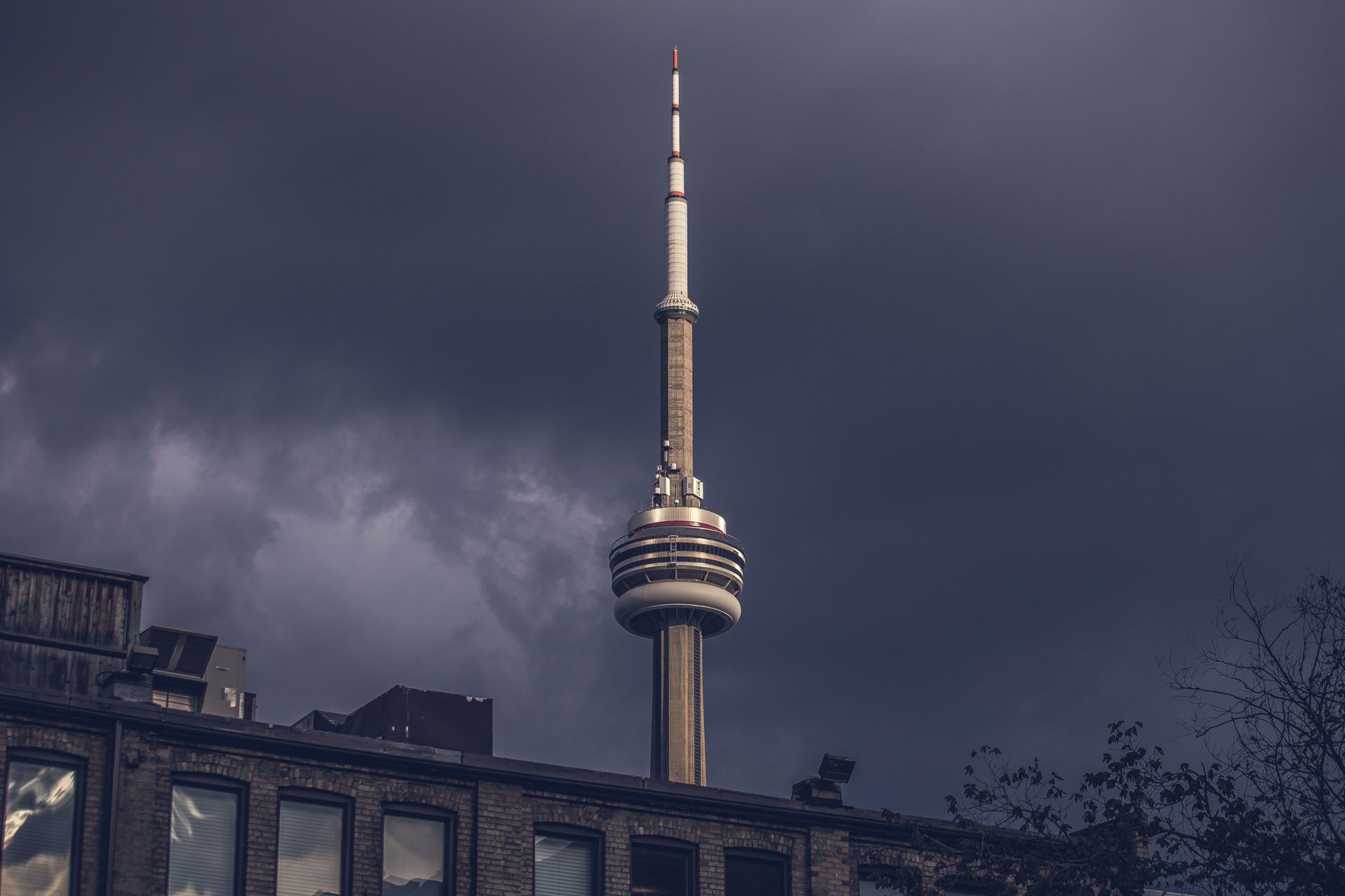 The CN Tower in Toronto set against a dramatic dark, stormy sky captures a modern urban landmark.
