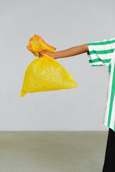 A person extending arm holding a yellow plastic bag, promoting waste awareness.