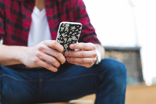 Casual young adult with smartphone, patterned case, and plaid shirt outdoors.